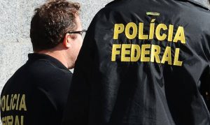 Dois agentes da Polícia Federal de costas. Imagem foca no nome 'Polícia Federal' que está atrás da farda de um deles