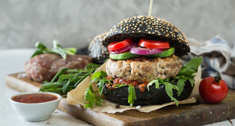 Descrição: hambúrguer vegano, com carne de origem vegetal grelhada e molho natural de tomate e vegetais complementando a iguaria.