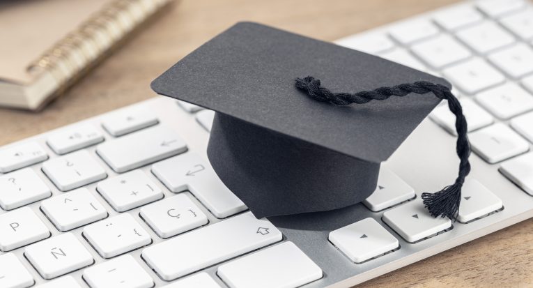 E-Learning or home study concept. Graduation cap on computer keyboard on wooden desk