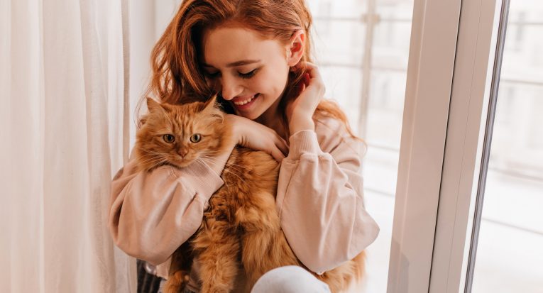 Relaxed smiling girl playing with her fluffy cat. Indoor shot of amazing lady holding pet.