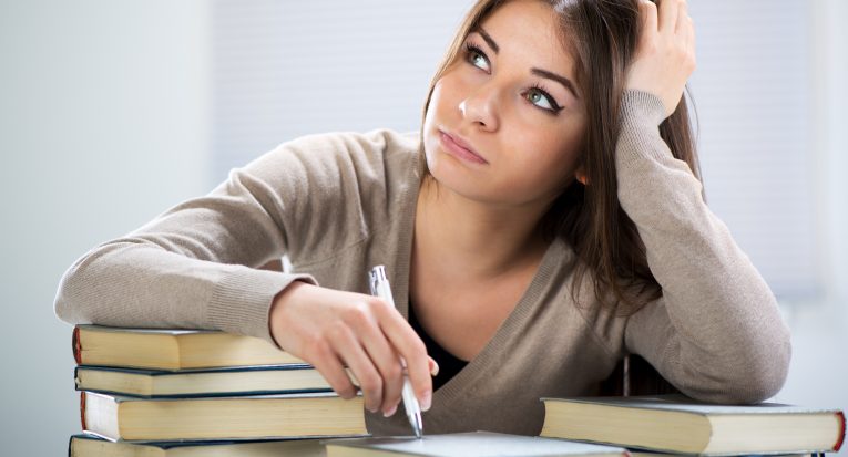 Tired student sitting with many books, with her head in hand.