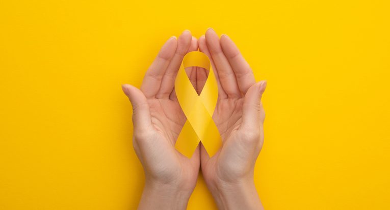 Partial view of female hands with yellow awareness ribbon on colorful background, international