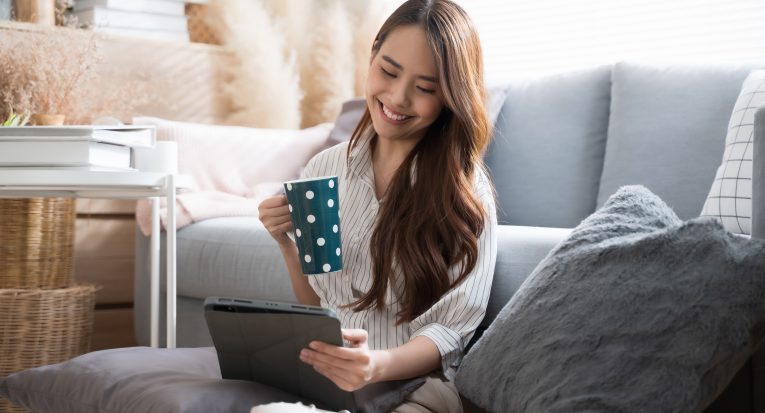 Asian woman happily using tablet to watch comedy series at home