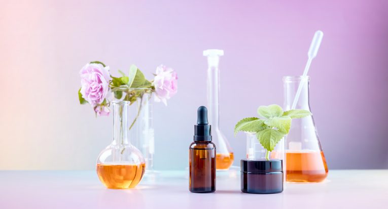 bottles for cosmetics, laboratory beakers, rosehip flower and mint leaves on a gradient background. the concept of natural cosmetics