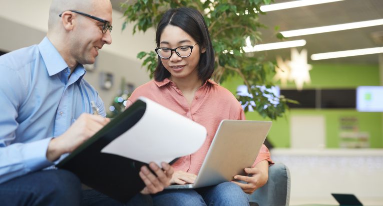 Portrait of young Asian businesswoman talking to manager while working on internship project, copy space