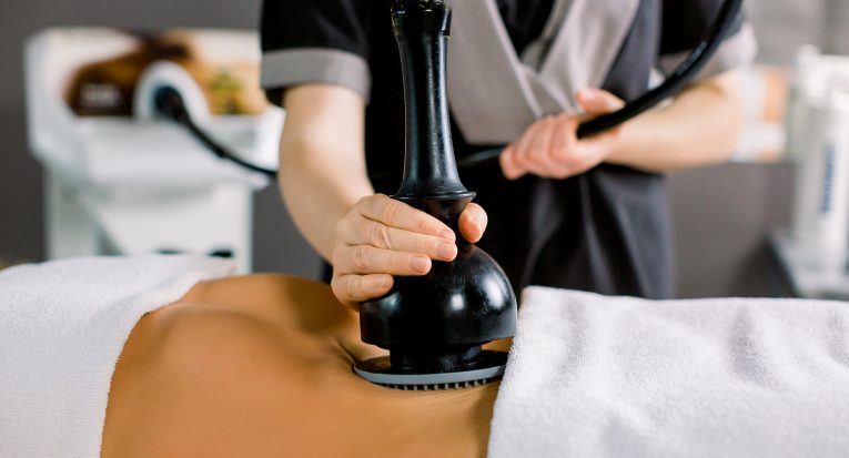 Vacuum massage device, anti cellulite body correction. Cropped image of woman client receiving vacuum massage of the abdomen and hands of female doctor holding the device.