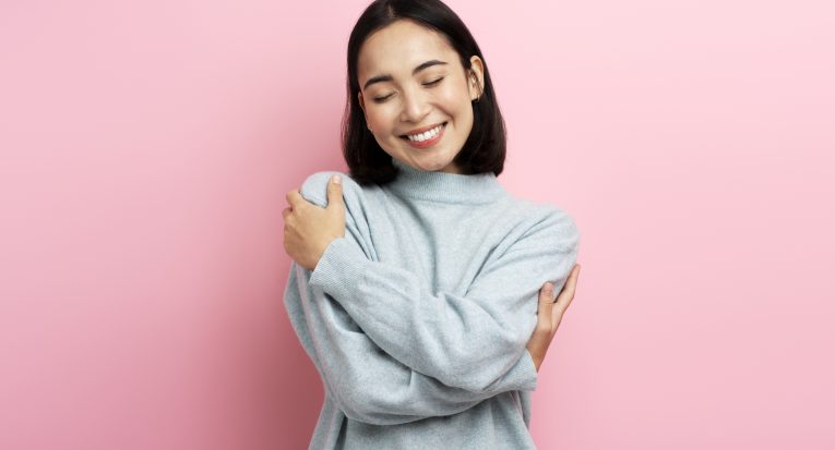 I love myself! Portrait of self-satisfied egoistic woman embracing herself and smiling with pleasure, feeling self-pride. Studio shot isolated on pink background