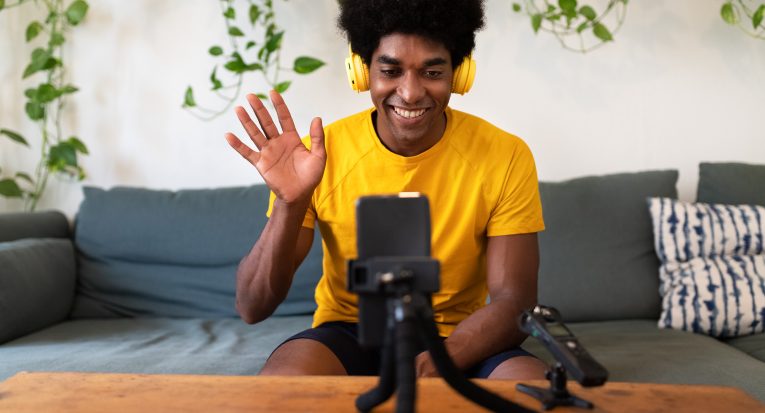 Young african american influencer waving hello to followers. Recording himself for video tutorial with mobile phone. Blogging concept.