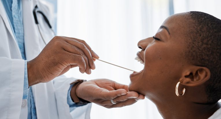 Doctor, otolaryngologist or dentist with a medical instrument checking the throat for tonsils or or.