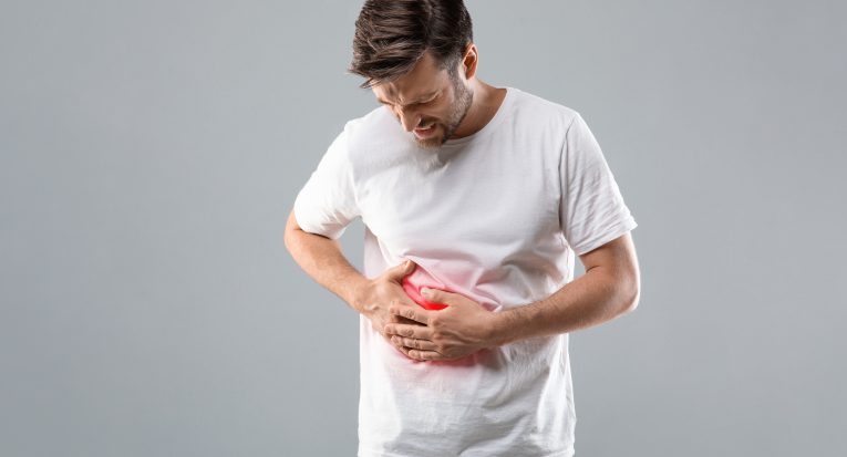 Middle-aged man holding his lightened with red right side, suffering from liver pain, grey studio background, copy space. Sad man having cirrhosis, rubbing his right side. Liver diseases concept