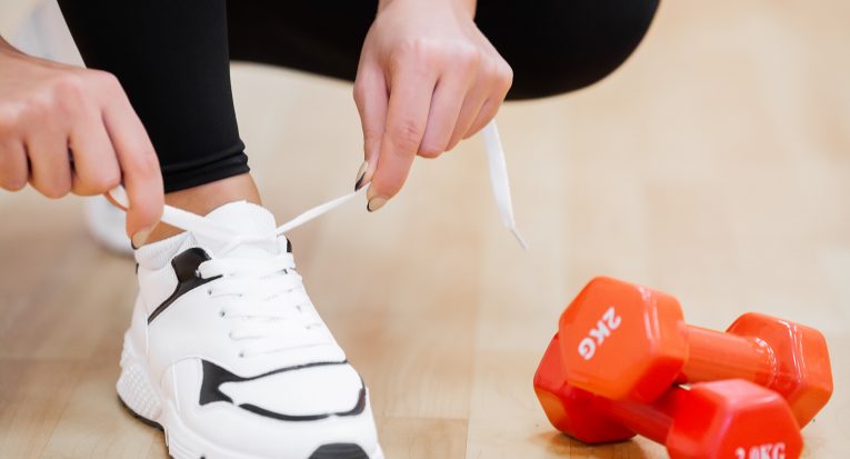 Physical activity. Close-up of girl tying shoelaces on sports shoes in gym.