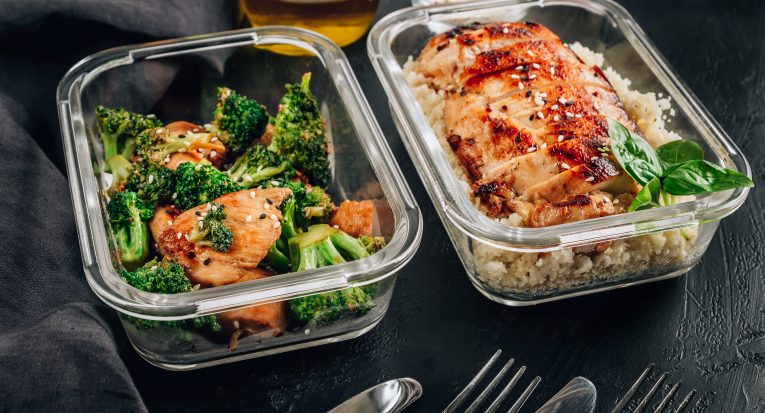 Keto lunchboxes - grilled chicken with cauliflower rice and chicken and broccoli in soy sauce with sesame seeds on a black table. Selective focus