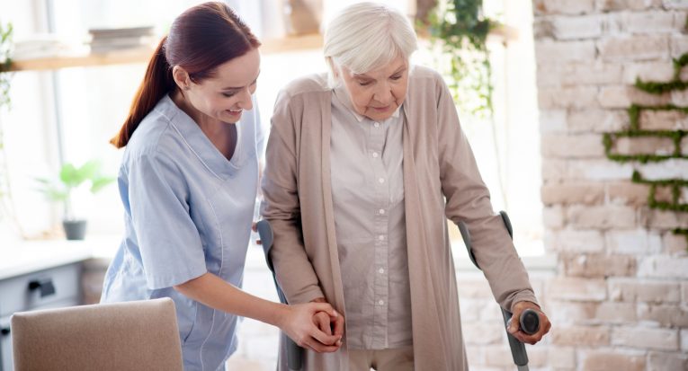 Assisting woman. Helpful caregiver smiling while assisting woman with crutches