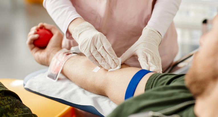 Close up of male donor giving blood at donation center with nurse helping, copy space