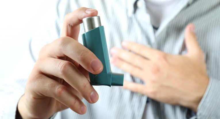 Young man holds asthma inhaler during asthma attack