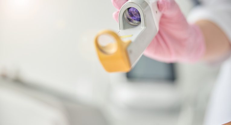 Cropped photo of a woman hand in a latex glove holding a laser device over the patient leg