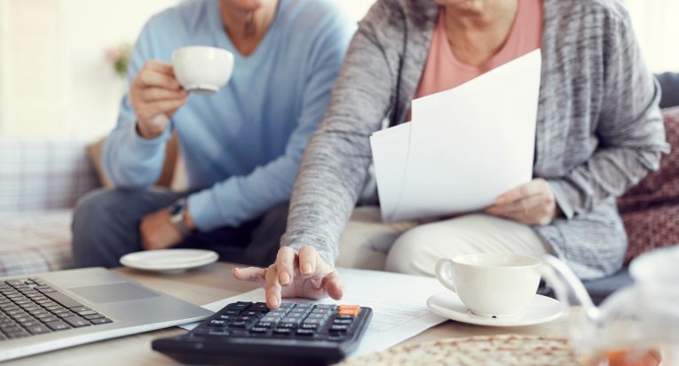 Close-up of married senior couple sitting at coffee table and using calculator while thinking how to save money