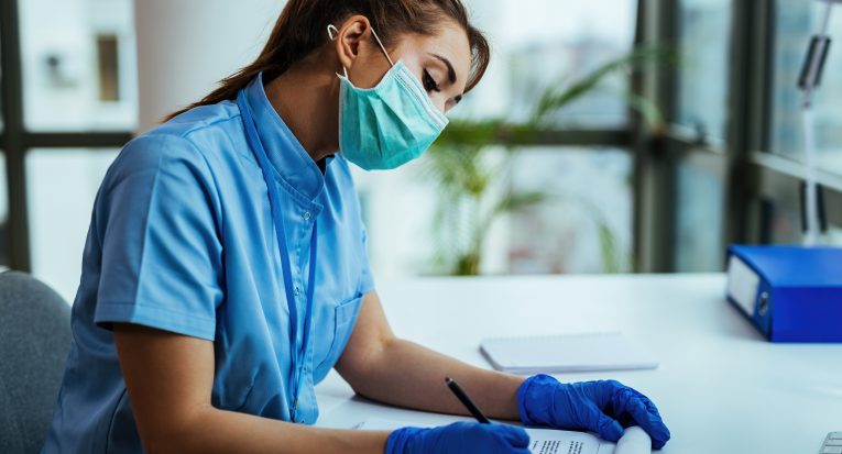 Female scientist doing on medical research and writing data while working during virus epidemic in a hospital.